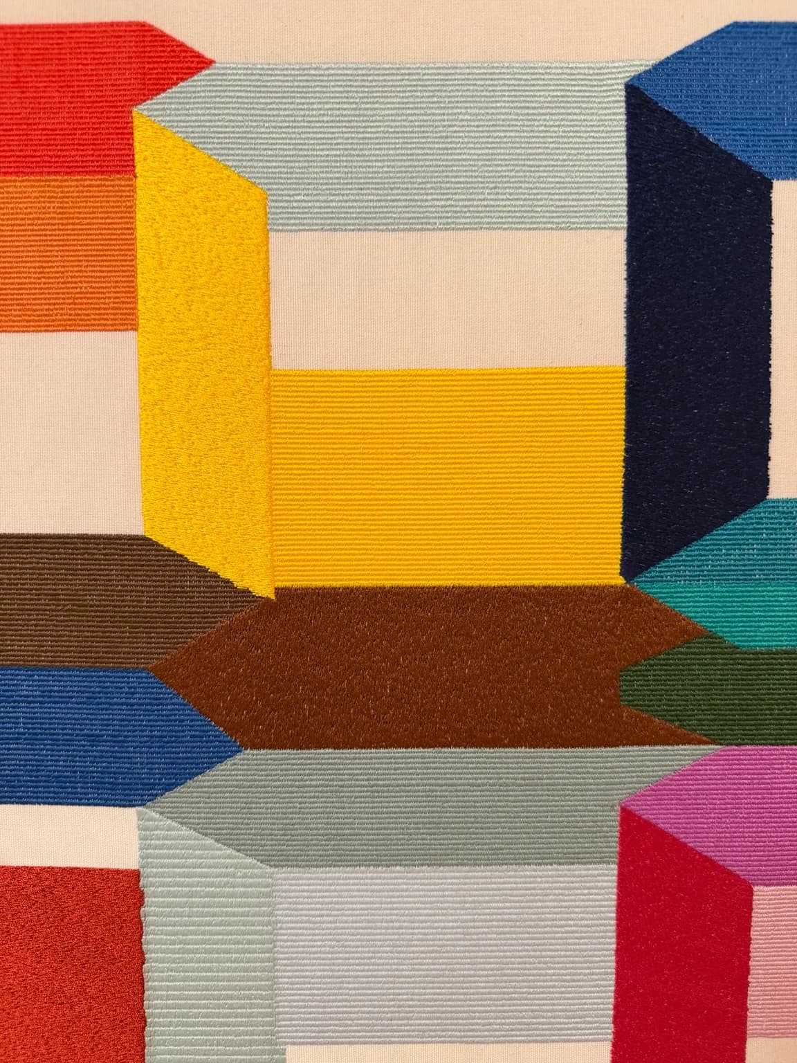 Where Colour Becomes Space (detail) — close-up of contrasting planes in red, blue, yellow, green, pink and neutral tones, defined by stitch direction